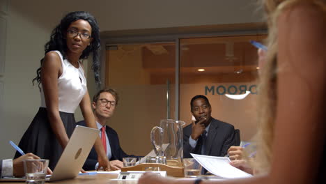 Young-black-woman-stands-to-address-team-at-business-meeting