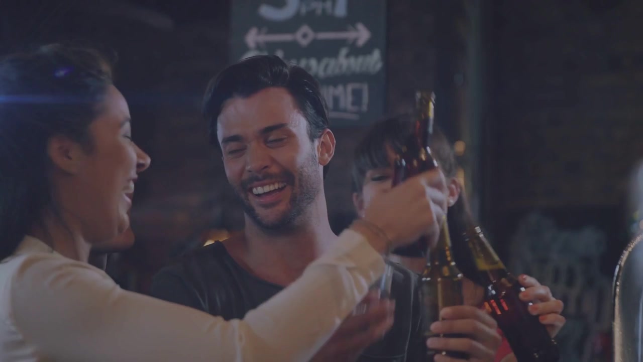 Gruppo che alza le bottiglie per brindare al bar, facendole tintinnare, avvicinandosi e sorseggiando per celebrare l'amicizia.