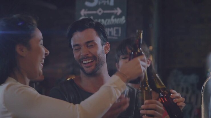 Gruppo che alza le bottiglie per brindare al bar, facendole tintinnare, avvicinandosi e sorseggiando per celebrare l'amicizia.