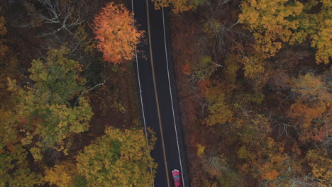 Drone-flying-over-two-lane-highway-in-New-England-in-the-fall-with-leaves-changing-colors