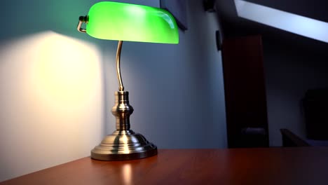 green reading lamp, glowing with a yellow light on the brown desk