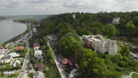 Backwards-aerial-view-of-the-beautiful-Kazimierz-castle-on-a-hill-between-green-trees