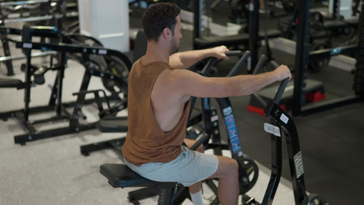 hombre común en forma trabajando en una máquina de fila sentada en un gimnasio moderno, hombre barbudo haciendo ejercicios de entrenamiento de músculos de baja latitud