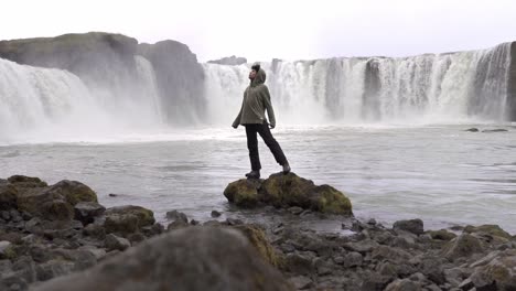 turista de pie en piedra cerca de una cascada espumosa