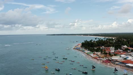 Absteigende-Luftdrohne-Weitwinkelaufnahme-Des-Hafens-Von-Porto-De-Galinhas-Oder-Hühnerhafen-Mit-Verankerten-Segelbooten-Und-Touristen,-Die-Im-Kristallklaren-Meerwasser-In-Pernambuco,-Brasilien,-Schwimmen