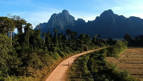 Sany-Road-Con-Dos-Motociclistas-Hacia-Montañas-Verdes-En-Laos-Mientras-El-Dron-Vuela-Alto-Y-Durante-El-Cielo-Azul