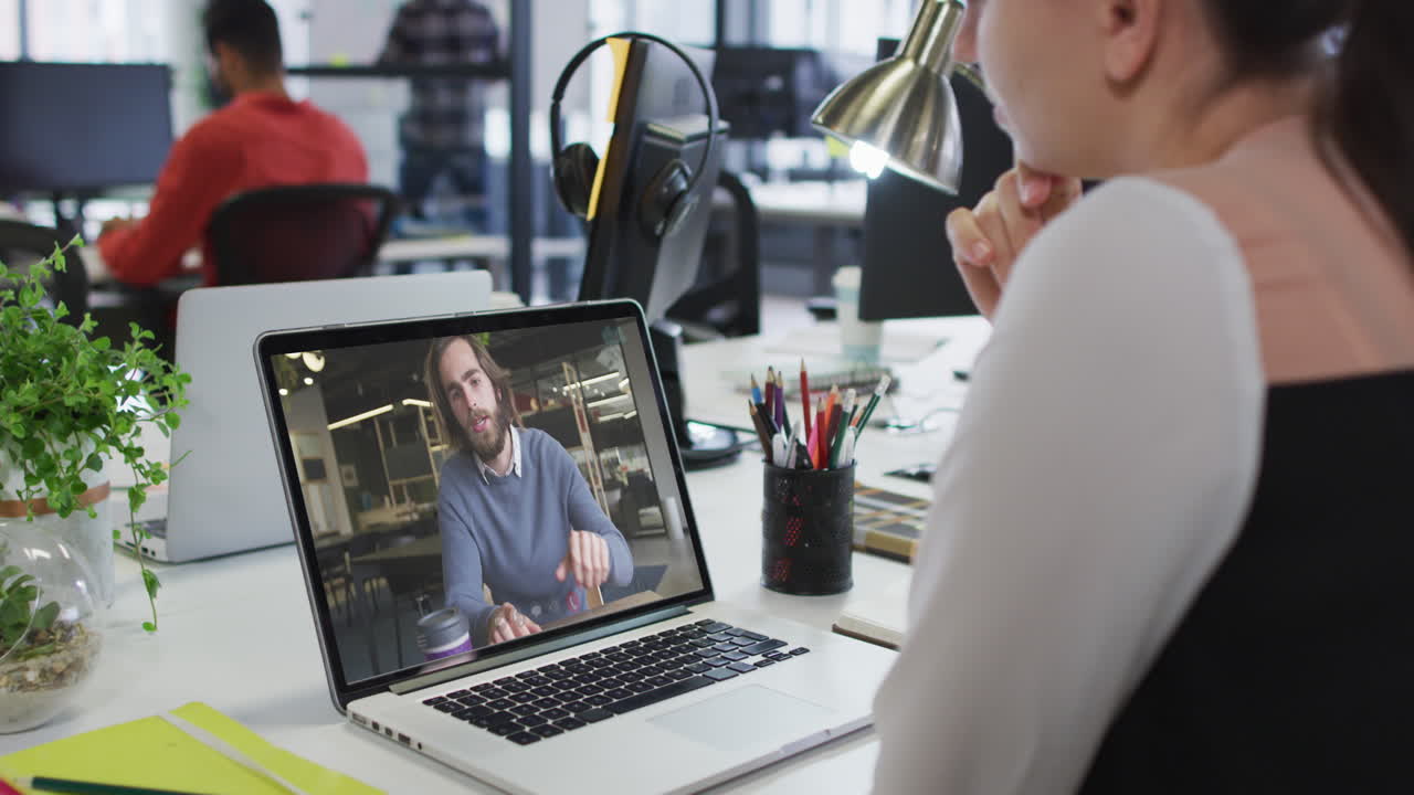 Caucasian woman having a video call on laptop with male colleague at office