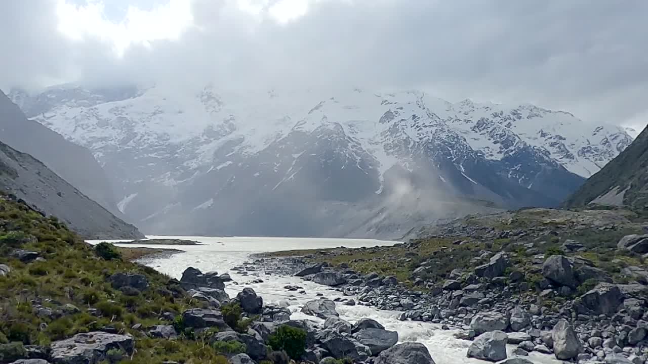 En timelapse af en bjergscene med jord, der blæses af vinden op ad en bjergryg, og en hurtigt strømmende flod.