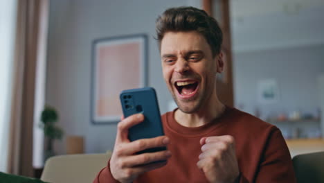 emotional guy rejoicing cellphone message at home close up. winner receive news