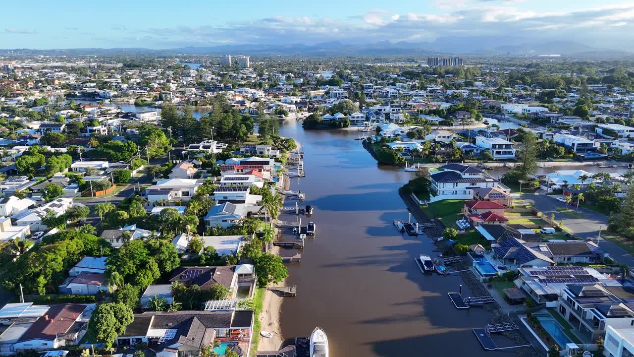 Aerial footage captures scenic riverfront houses in Broadbeach, Gold Coast, under clear skies with vibrant greenery and waterways