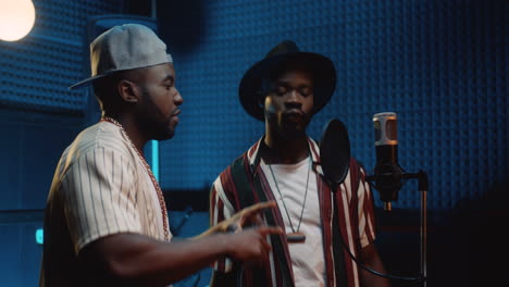 Two-Young-Guys-Rappers-Reading-Rap-In-The-Mic-While-Recording-A-Song-Together-In-The-Sound-Studio