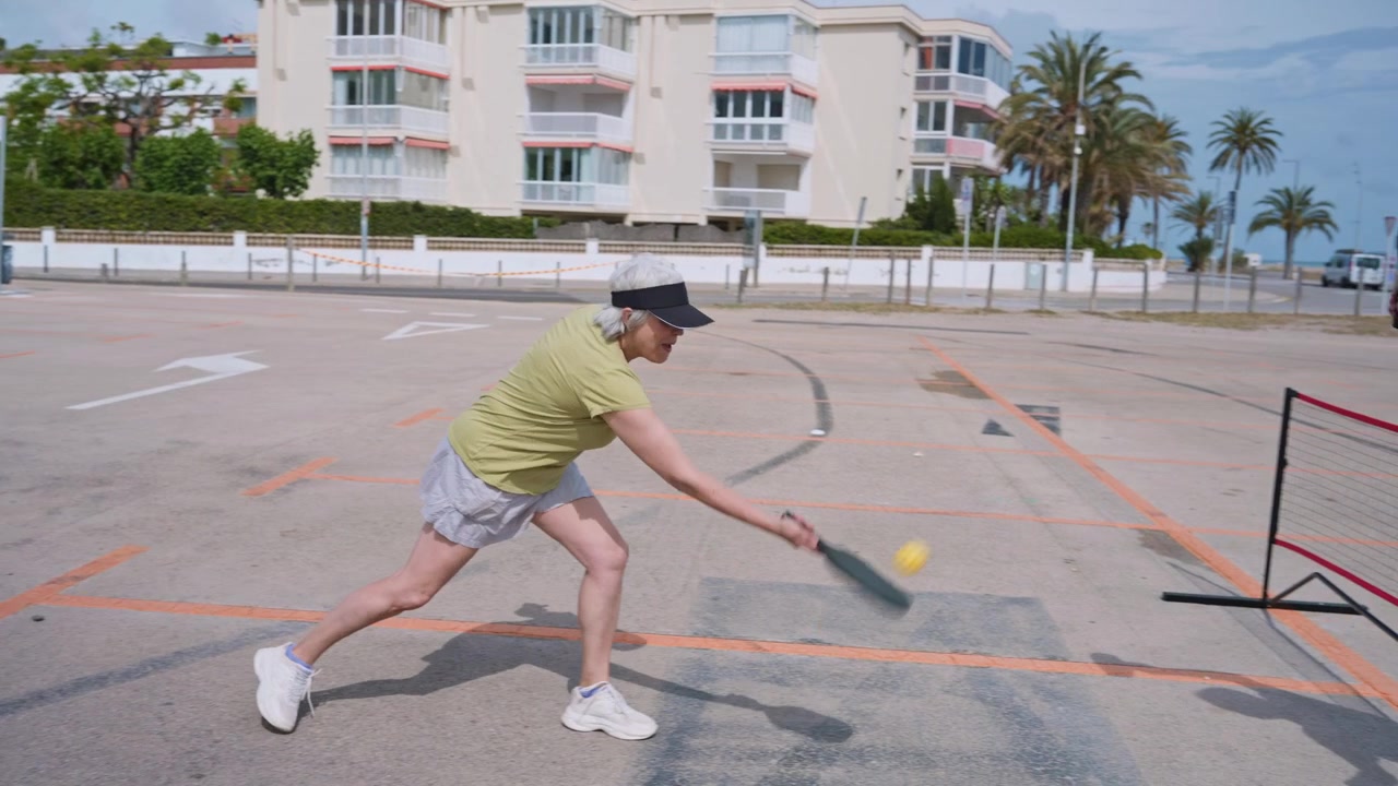 Pareja de adultos mayores activos jugando pickleball al aire libre en un día soleado.