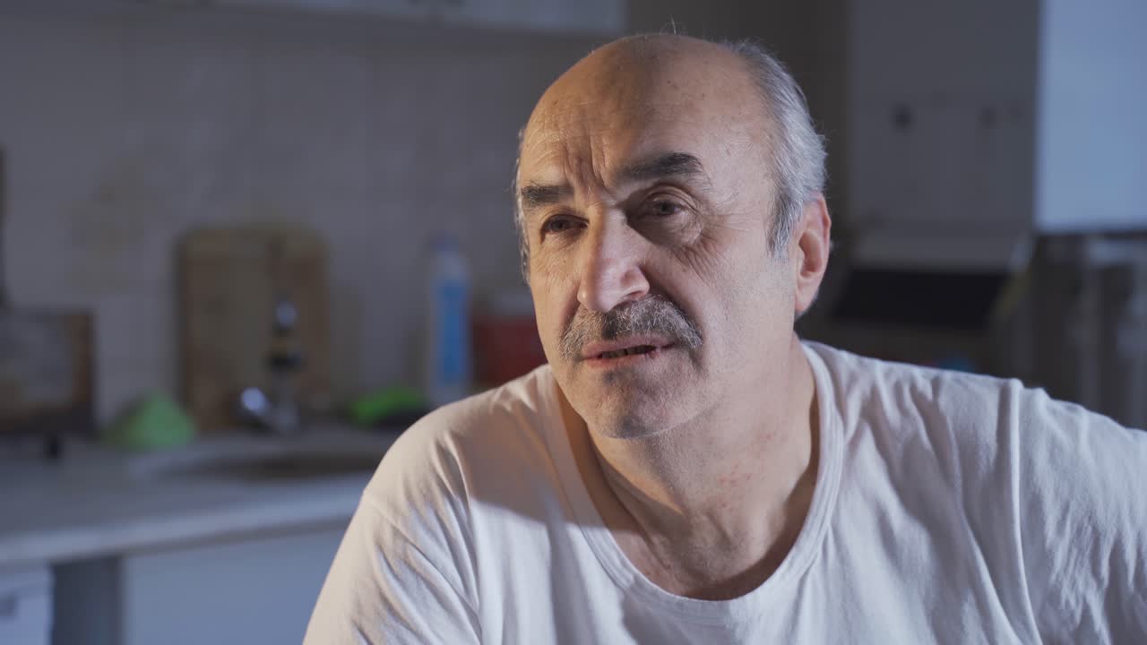 un viejo deprimido y triste sentado solo en la cocina pensando.