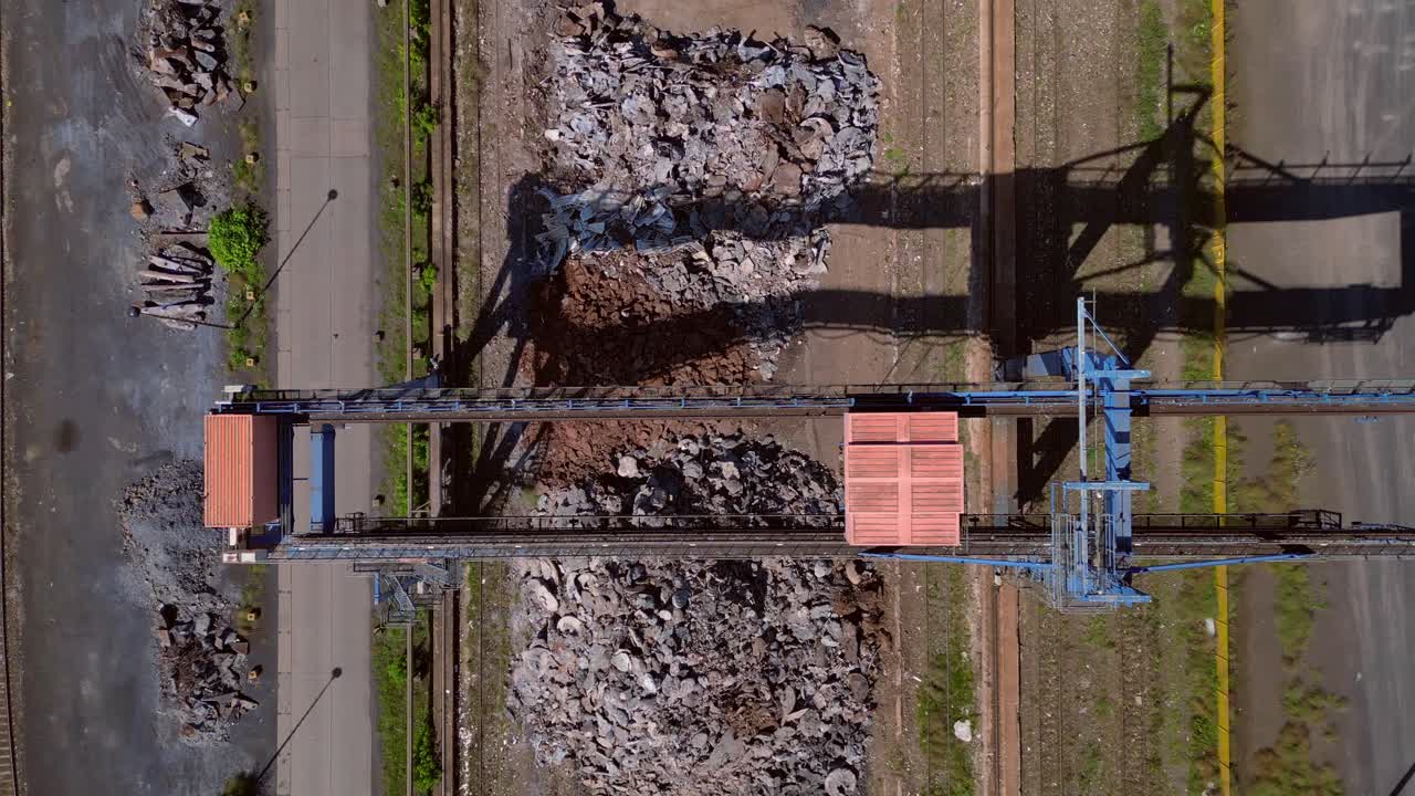 Gantry crane transporting scrap metal at Hennigsdorf electric steel mills on a sunny summer day. Smooth aerial view flight vertical bird's eye view ascending drone