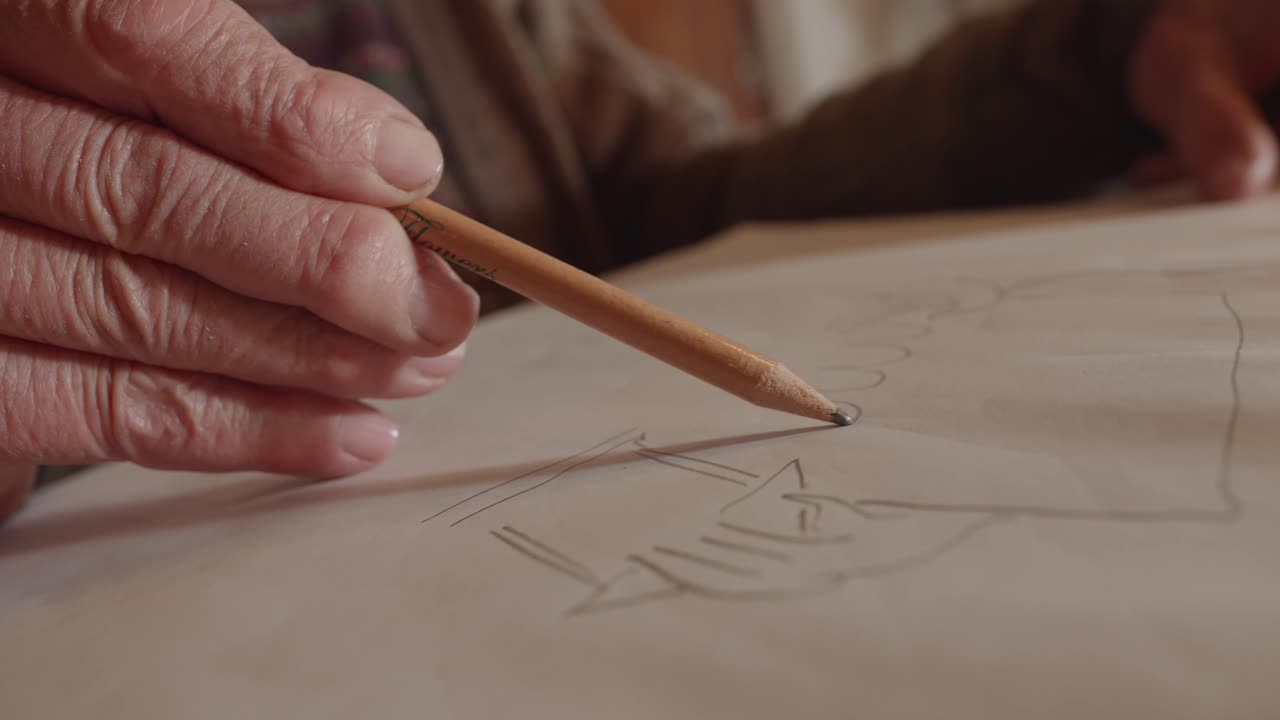 Elderly hand of an ancient artist sketching architectural draft with pencil on paper.
