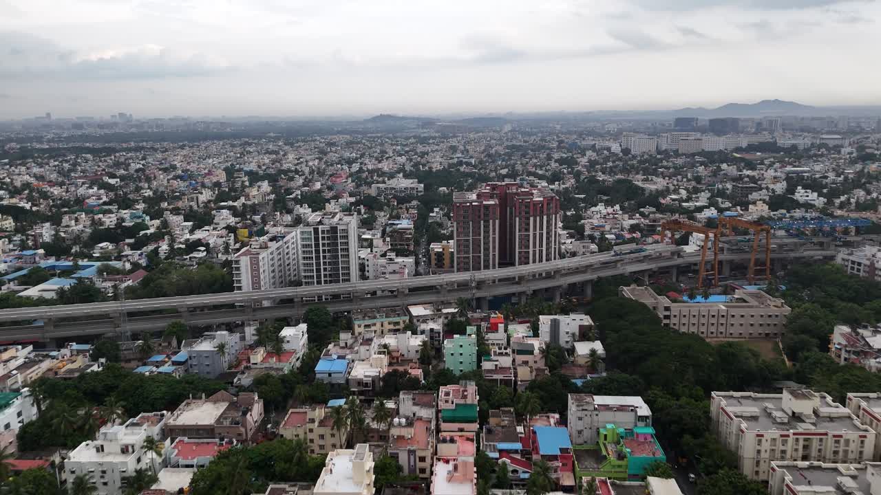 Aerial footage captures the dynamic transformation of Chennai under a dramatic monsoon sky. Dark rain clouds loom over the city as the Metro Phase 2 construction