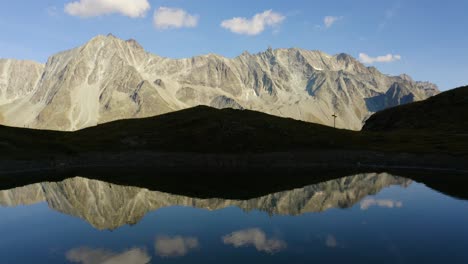 Flying-low-and-sideways-above-perfect-mirror-lake-with-high-mountain-peak-in-the-background-Autumn-colors-in-Arolla,-Valais---Switzerland