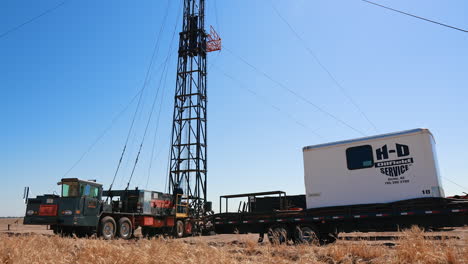 a truck with attached derrick for drilling the oil in the field. man in helmet stands on the vehicle setting the equipment for work.