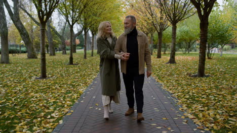 charming elderly man and beautiful woman looking each other in autumn park.