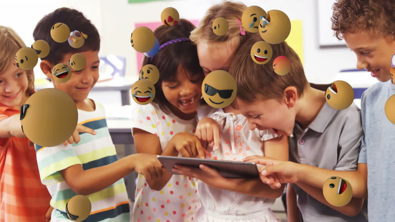 Animation of emoticons floating over diverse children laughing and using digital tablet in classroom