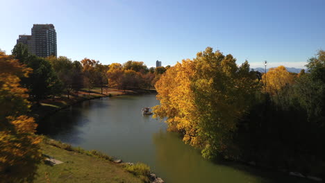 establishing wide aerial drone shot flying low over lake and fall trees revealing denver city on a summer's day