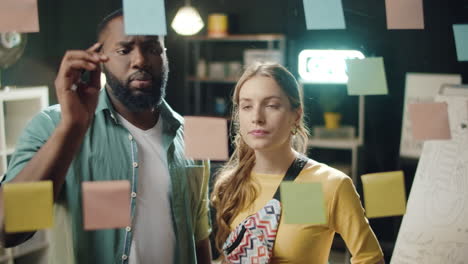 Closeup-focused-multi-ethnic-couple-looking-at-stickers-in-hipster-office