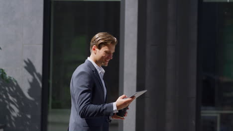 trabajador financiero sonriente comprobando el teléfono inteligente caminando en un lugar de trabajo moderno afuera.