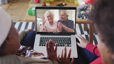 african american mother and daughter using laptop for christmas video call with couple on screen