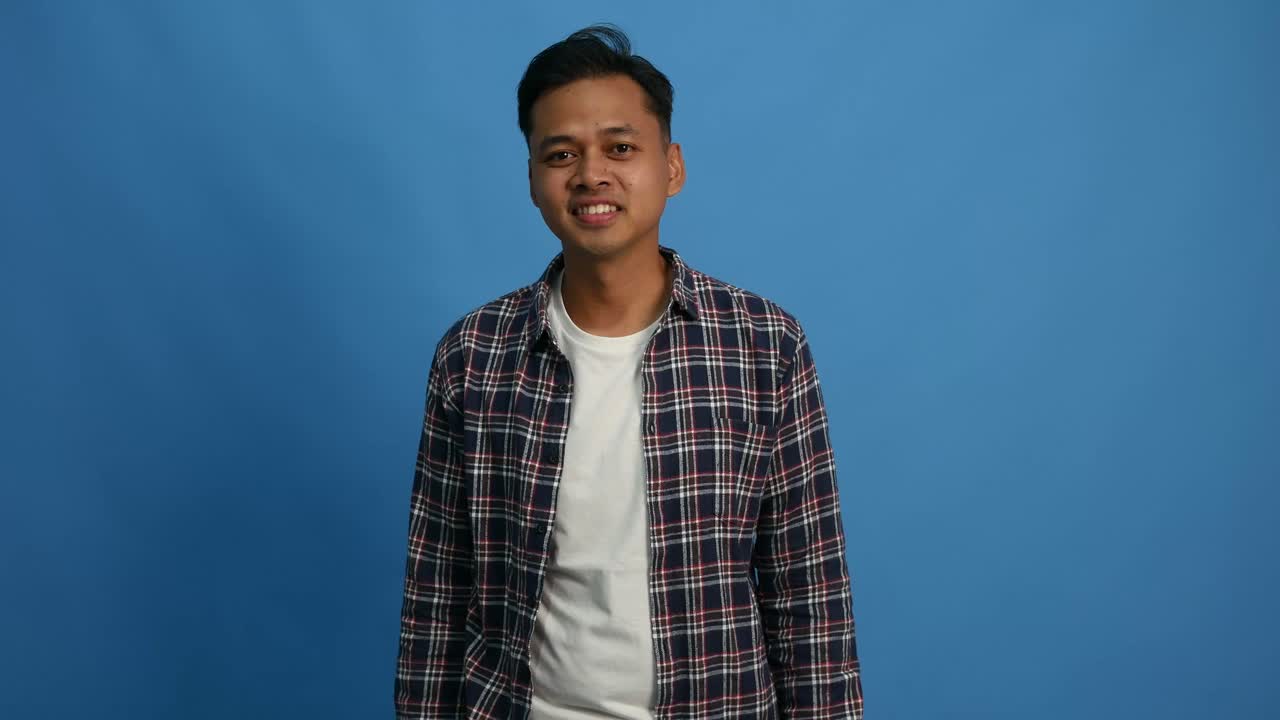 Happy asian man dancing celebrating success while raising fists isolated on blue background