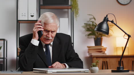 elderly caucasian businessman grandpa in suit working having mobile phone talk at home office desk