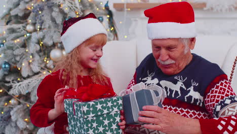 Granddaughter-exhcanging-Christmas-gift-present-boxes-with-amazed-happy-elderly-grandfather-at-home