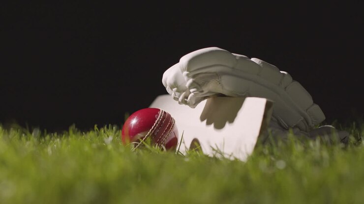 Natura morta di cricket con primo piano di mazza, palla e guanti nell'erba