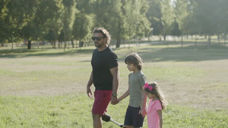 side view of dad with artificial leg strolling with kids in park