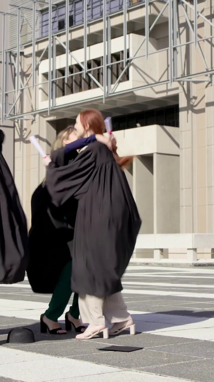 Video verticale: Una rossa che cammina in toga, si sistema il tocco e lo lancia nel campus, festeggiando con il diploma.