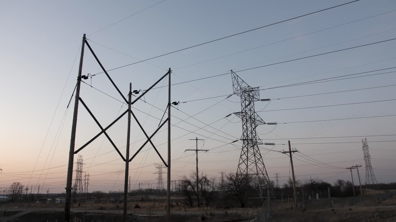 Transmission towers and electrical lines silhouetted with setting sun in background