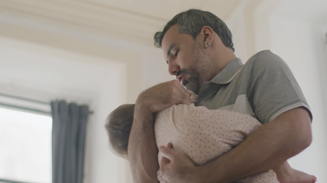 Loving Dad Cradling His Cute Baby Girl In His Arms At Home