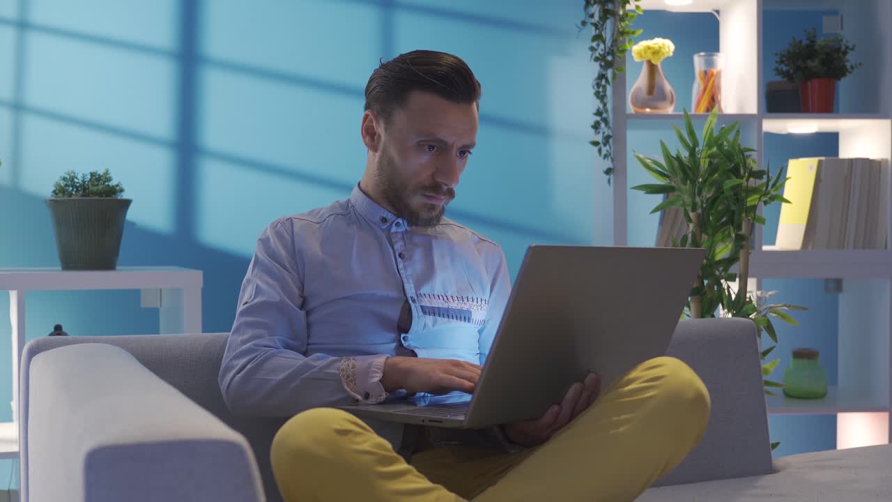 hombre elegante y elegante usando la computadora portátil por la noche de una manera seria y centrada en casa.