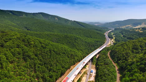 new highway through green hills. construction workers build a highway through lush green forests in a mountainous area under clear blue skies