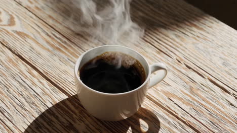 steaming hot black coffee in a white mug on a wooden table