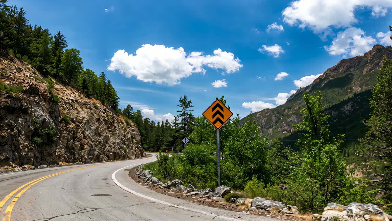 Approaching left bend, dashcam navigating rocky canyon road, showing yellow chevron and merge signs