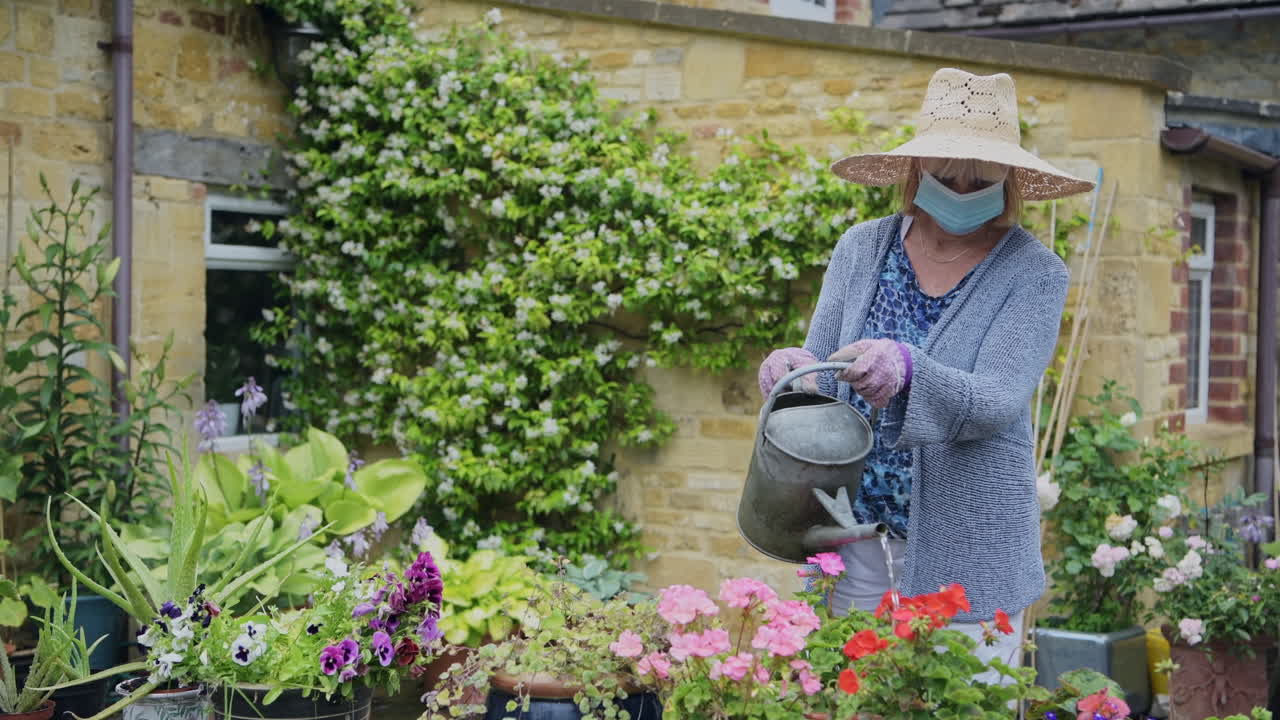 Adult woman watering her garden, gardening during coronavirus pandemic lockdown and wearing face mask