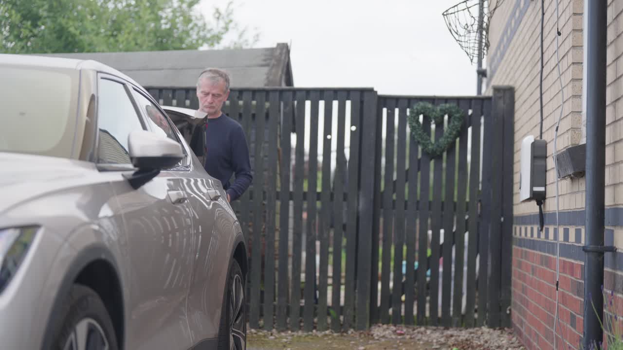 Man retrieves electric cable, vehicle boot opened, home charge point