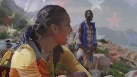 animation of american flag over smiling diverse couple sitting in mountains