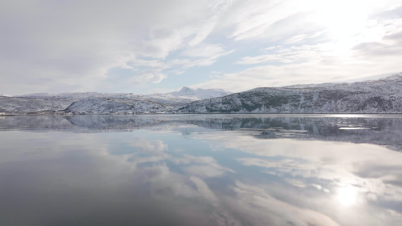 노르웨이의 눈 덮인 산 경사면과 하늘을 반영하는 잔잔한 피요르드 바닷물