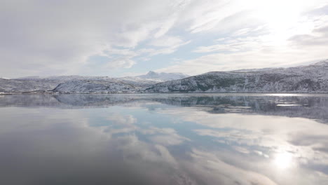 calm fjord sea water mirroring snowy mountain slope and sky in norway