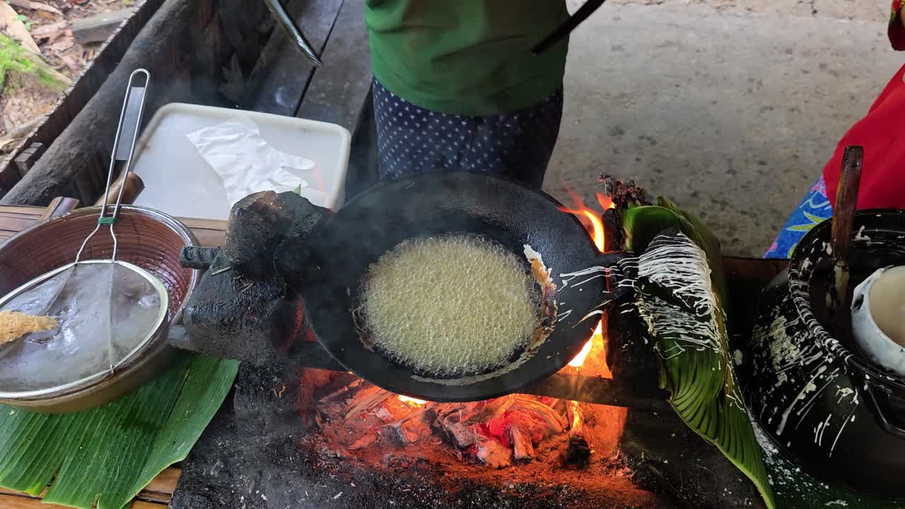 Women in traditional attire fry traditional Kuih Jala snack over an open fire during a cooking demonstration in Mari Mari cultural village, Kota Kinabalu, Malaysia - top down view