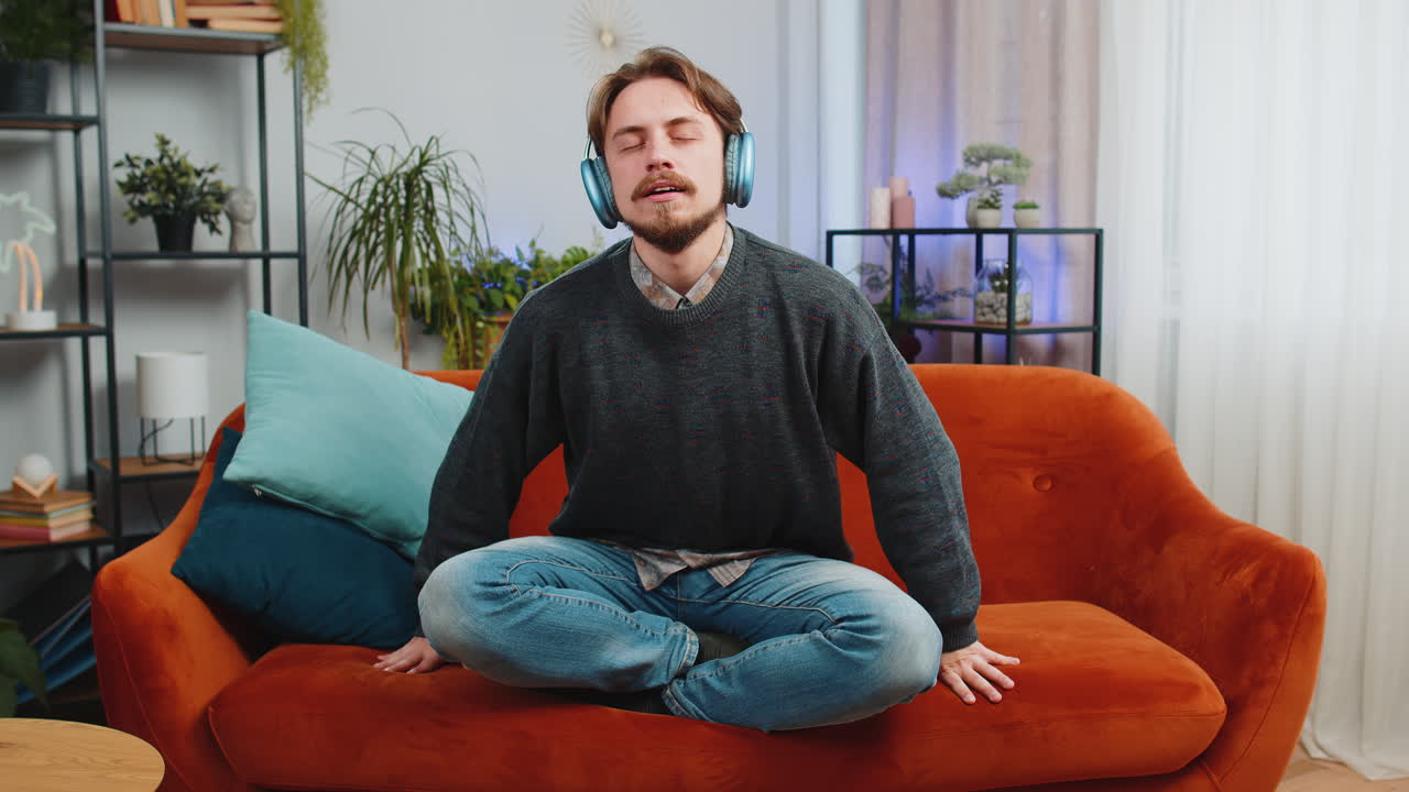 Bearded man listening music breathes deeply meditating with concentrated thoughts peaceful at home
