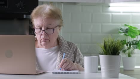 senior woman in glasses working using laptop with serious face at home