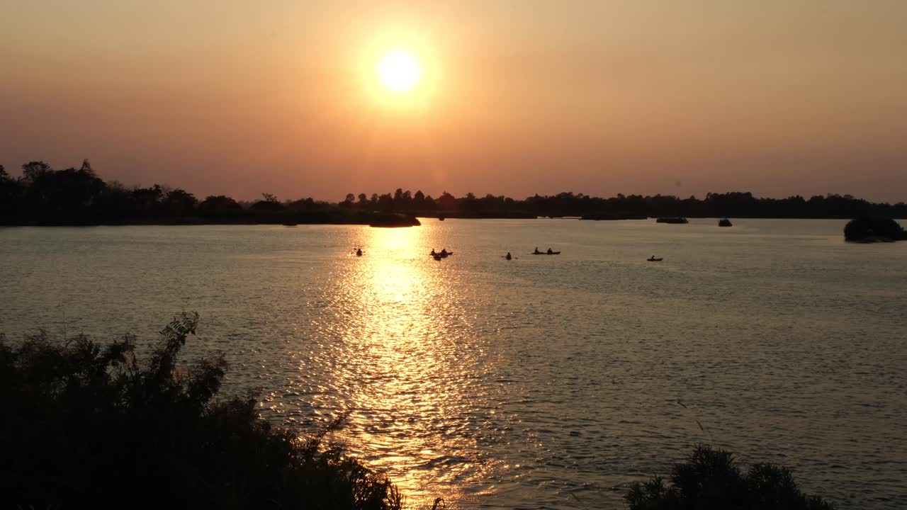 las imágenes de 4k muestran el pintoresco y dramático paisaje a lo largo del río mekong en laos, con barcos en miniatura en el telón de fondo de una impresionante puesta de sol
