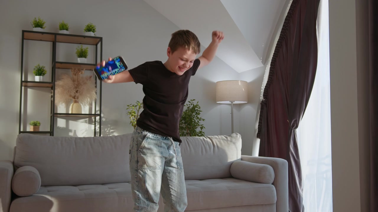 Young boy energetically dancing with arms outstretched in a bright sunlit room expressing pure